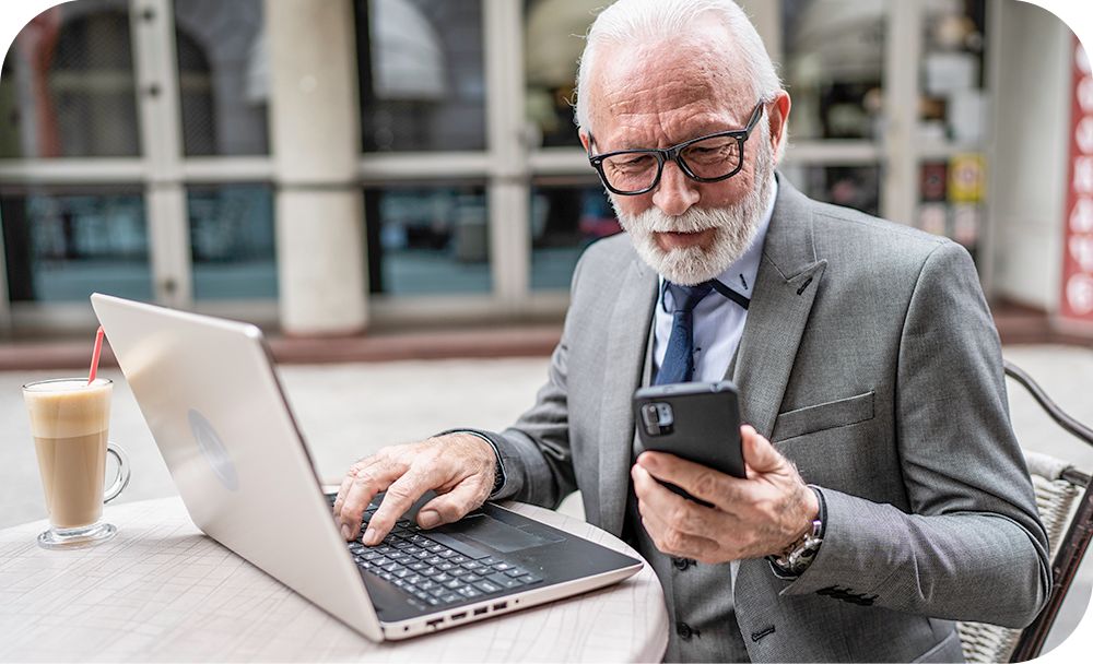 Man sits outside while working from a phone and laptop