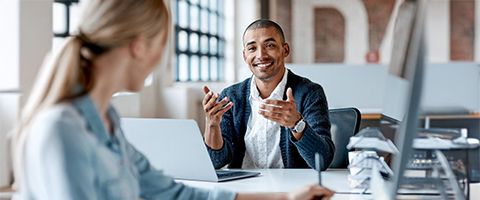 Two professionals sit across at able having a conversation with a laptop between them