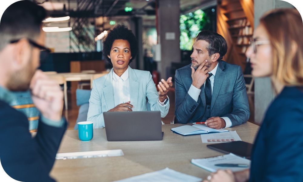 Four people have a conversation at a desk