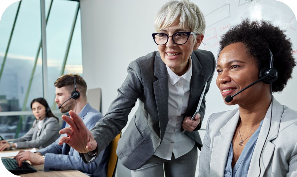Woman in a gray suit standing in a row of three employees working with headsets on